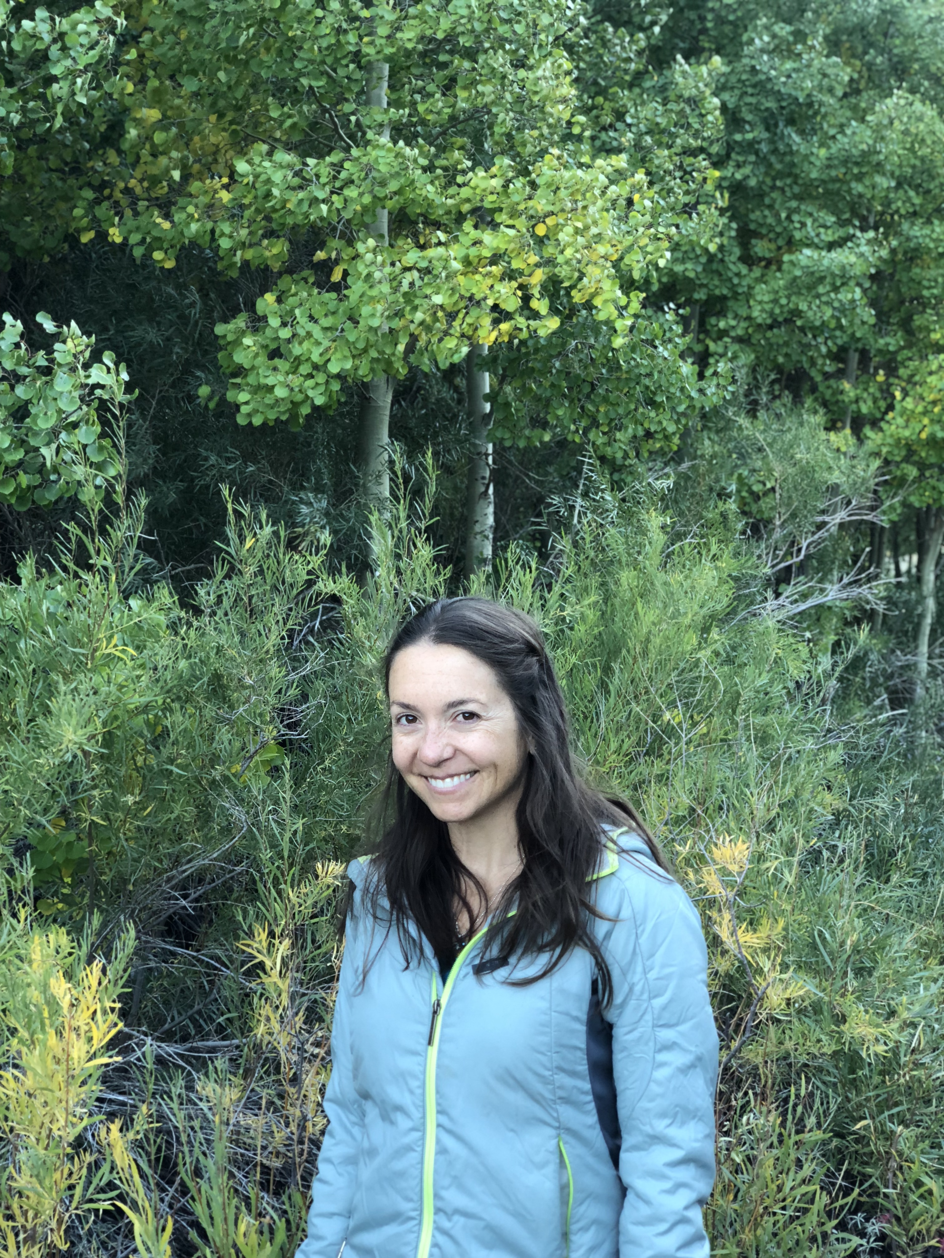 Attorney Sophie Bidet wearing a blue coat standing in front of an aspen forest smiling